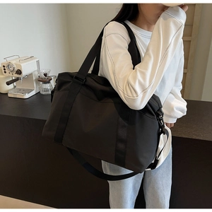 Detail of a black large capacity travel duffel bag with handles and adjustable shoulder strap