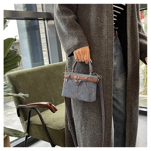 Detail of light blue denim box bag with brown leather trim and retro buckle accents