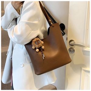 Brown litchi grain tote bag with plush lion charm shown on a white blazer outfit