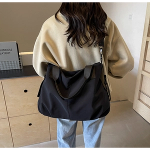 Rear view of a model carrying a large black nylon tote bag in a minimalist interior