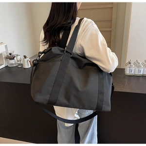 Man carrying a large black travel duffel bag in a modern cafe setting showing rear view