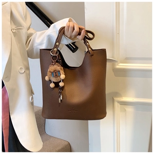 Detail of dark brown pebble leather bucket bag with plush charm and gold logo