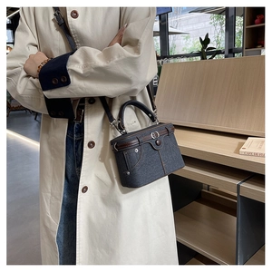 Detail of blue denim box bag featuring vintage jeans stitching and brown leather handles