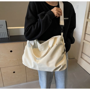 Detail of white canvas tote bag with wide shoulder strap and black metal buckle on model