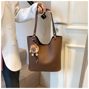 Detail of dark brown lychee leather tote bag with a cute plush lion charm accessory