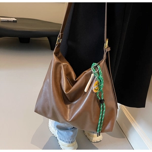 Détail d'un grand sac cabas marron avec un pendentif smiley vert et boucles dorées
