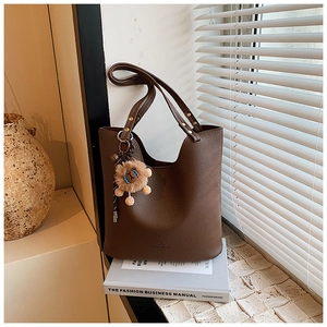 Detail of dark brown leather tote bag with plush lion charm on side straps