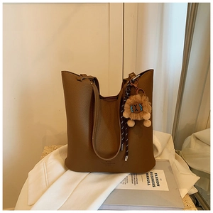 Detailed view of brown litchi grain leather tote bag with a plush lion keychain charm