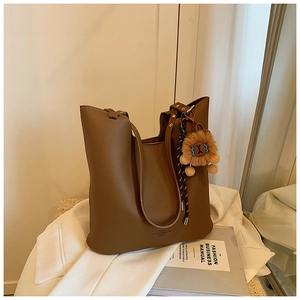 Detail of brown lychee leather tote bag with a cute yellow lion plush keychain
