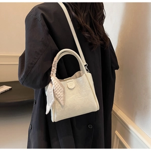 Creamy white bucket bag detail with woven handle and elegant scarf on a black coat