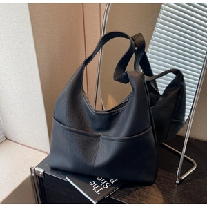 Detail of black pebbled leather texture and functional front pockets on a hobo tote bag