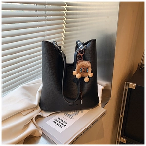 Black pebbled leather tote bag detail with brown plush mascot on a windowsill