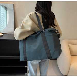 Detail of teal travel bag with black strap worn by a model in minimalist interior