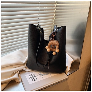 Detail of black pebbled leather tote bag with a plush lion charm on fashion magazines