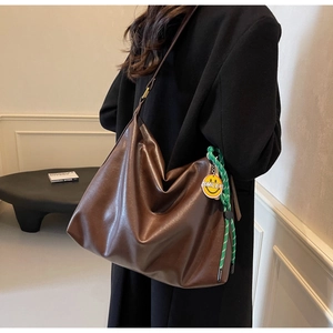 Détail du sac hobo marron foncé avec breloque tressée verte et étiquette smiley jaune