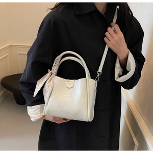 Close-up of beige leather bucket bag with textured finish and silk scarf on handle