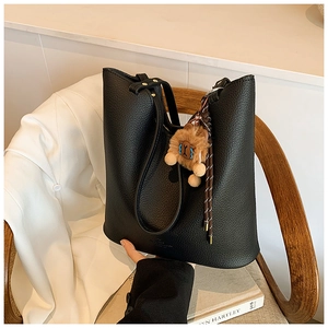 Close-up of black textured leather tote bag with a cute lion plush charm on a chair