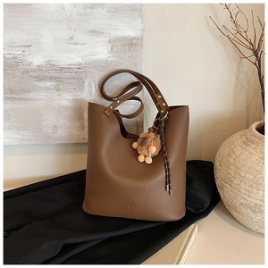 Detail of dark brown lychee grain leather bucket bag with plush charm and woven strap