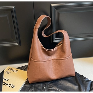 Close-up of brown pebbled leather tote bag with front pockets on a textured background