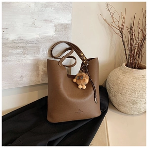 Close-up of brown pebbled leather bucket bag with a plush lion charm and gold hardware