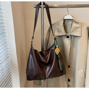 Détail du sac hobo marron foncé avec pendentif Smiley sur un trench-coat beige