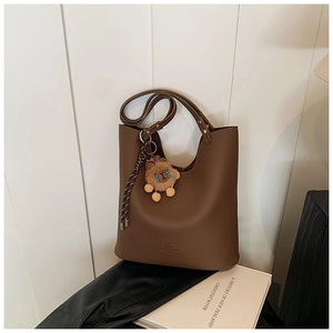 Close-up of brown textured leather bucket bag with cute bear charm and woven strap