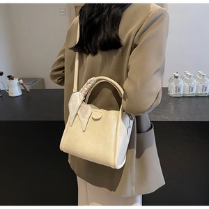 Close-up of creamy white tote bag with silk scarf detail worn by a model in a warm setting