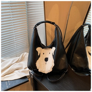 Detail of black leather tote bag featuring a white plush dog patch on a sleek dresser