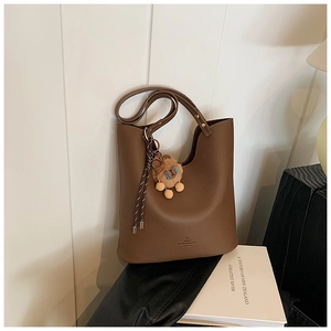 Close-up of brown litchi leather bucket bag with plush lion charm and golden accents