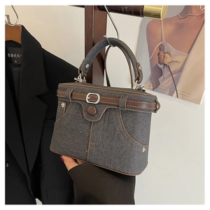Detail of grey denim handbag with brown leather trim hanging on a wooden rack