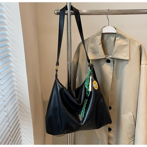 Détail du grand sac hobo noir avec pendentif smiley jaune posé sur un trench-coat