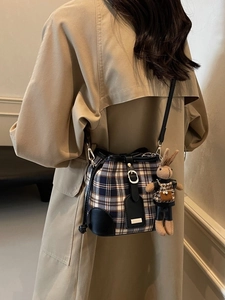 Elegante geruite emmertas met konijnenhanger gedragen door model in beige trenchcoat