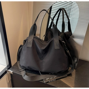Detail of black nylon tote bag with reinforced handles and adjustable strap in modern setting