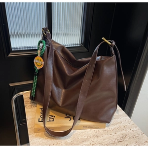 Détail du sac hobo en cuir marron foncé avec anneaux dorés et breloque smiley verte
