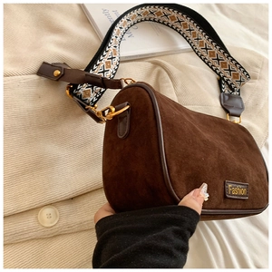 Detail of dark brown suede cylinder bag with ethnic embroidered strap and Fashion label