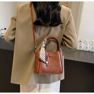 Brown vintage bucket bag detail with geometric silk scarf and adjustable strap on a model
