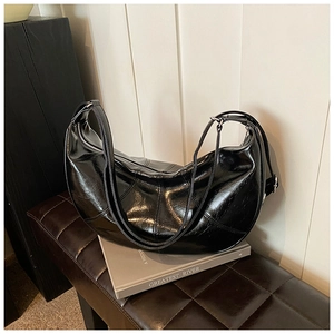 Detailed view of black patent leather half-moon bag with stitching on a leather bench