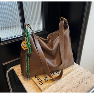 Détail du sac hobo en cuir marron foncé avec un charme tressé vert et pendentif sourire