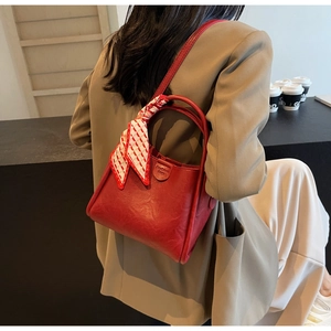Detail of red bucket bag with litchi texture and checkered scarf on model shoulder