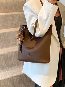 Dark brown pebble leather tote bag with plush bear charm worn by a model