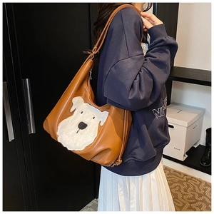 Close-up of brown textured leather hobo bag featuring a white plush dog patch design