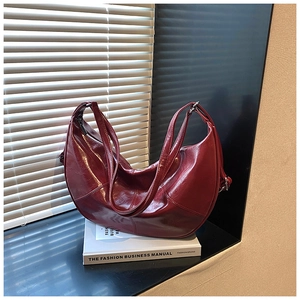 Close-up of a glossy burgundy crescent shoulder bag on a white decorative book