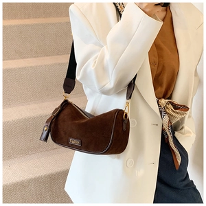 Detail of dark brown suede crescent bag with gold hardware and wide nylon strap on model