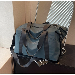 Detail of teal travel bag on wooden table with adjustable strap and metal hardware