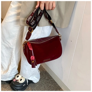 Detalle de bolso bandolera de ante burdeos con correa estampada y placa de metal