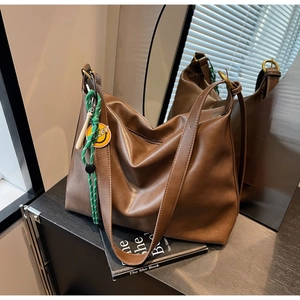 Détail d'un sac hobo marron avec charme smiley, bandoulière large et livre décoratif