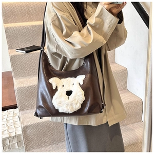 Detail of a brown leather shoulder bag featuring a white plush dog patch and adjustable strap