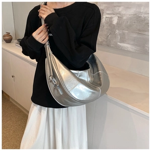 Silver crescent moon shoulder bag with metallic finish shown on model in a modern home
