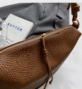 Detail of smooth metal zipper and rich lychee grain leather texture on brown crossbody bag