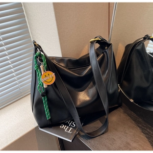 Détail du grand sac hobo noir avec boucle dorée et accessoire smiley tressé vert